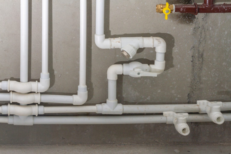 A plumbing system consisting of white pipes running along a basement wall.